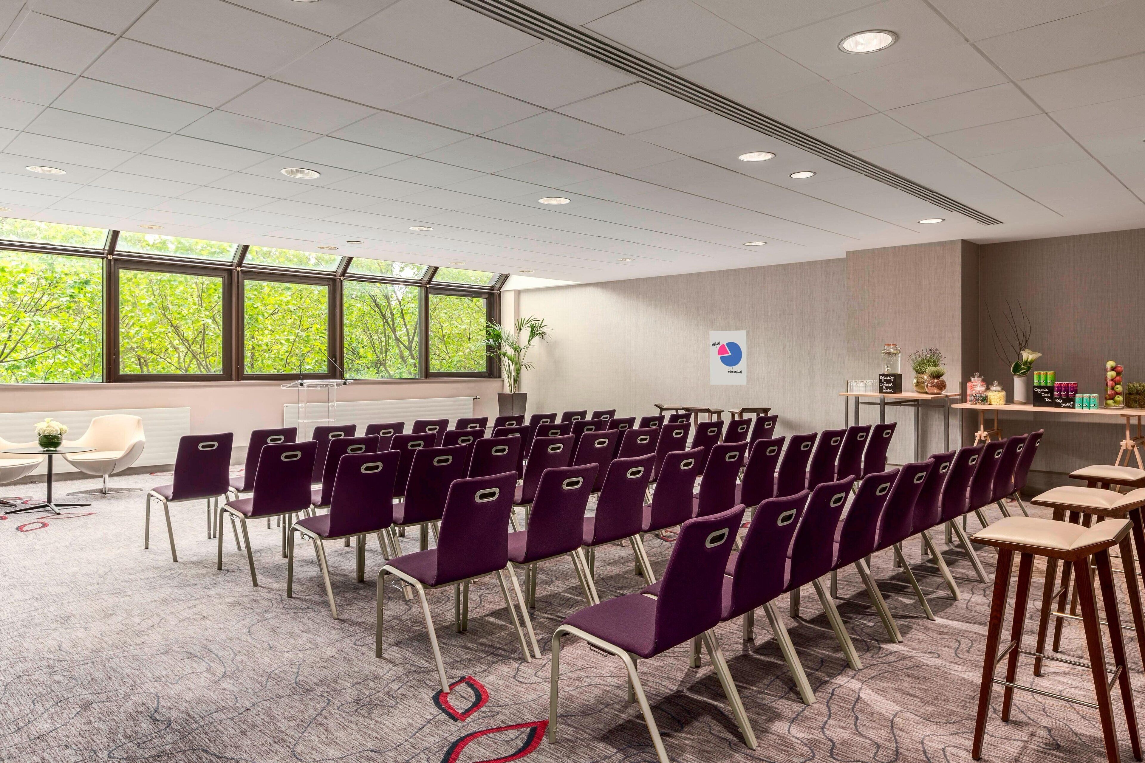 A conference room with rows of purple chairs, a whiteboard, and a window with a view of trees.