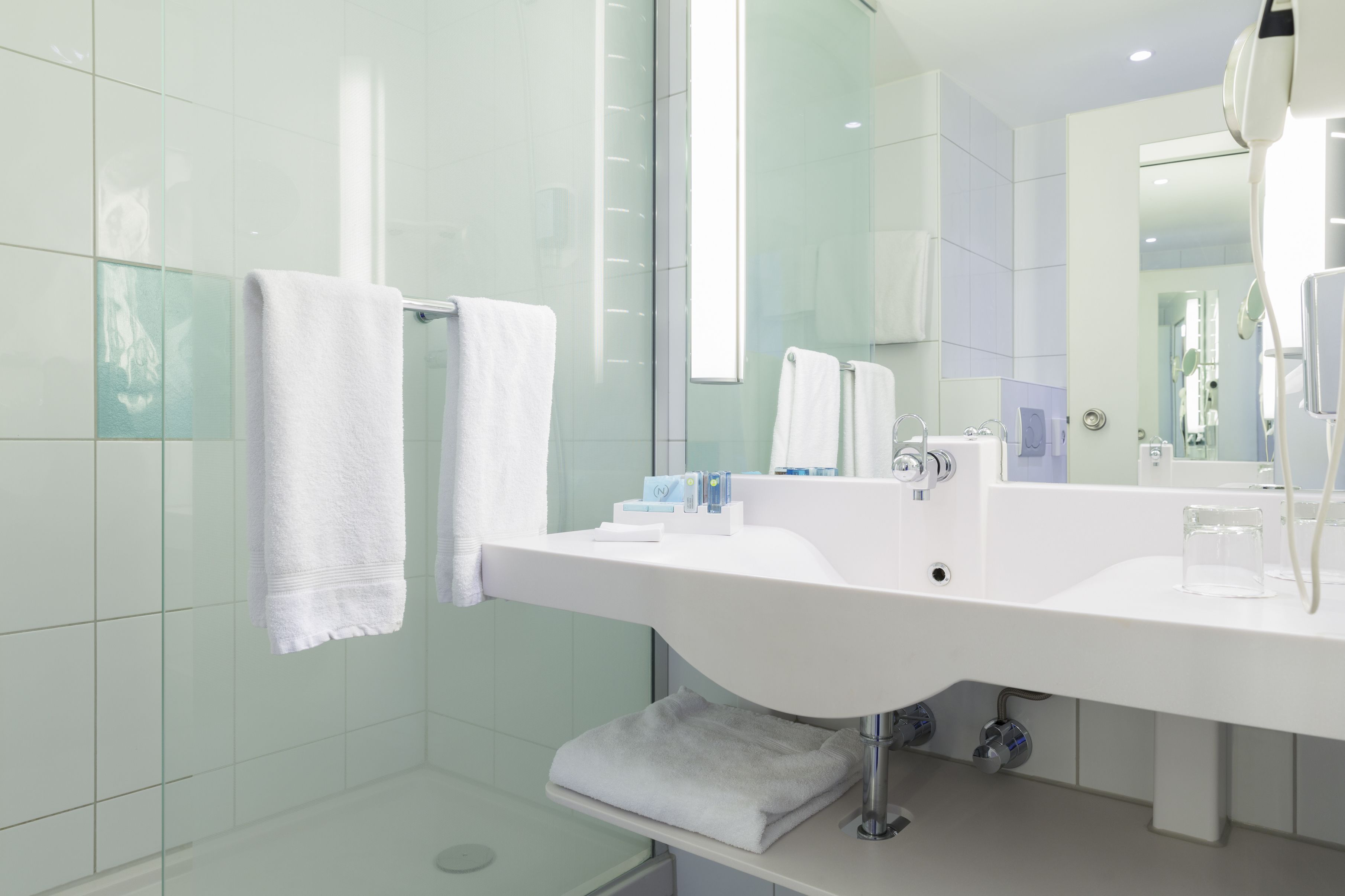 A modern bathroom with a white sink, a glass shower enclosure, and a towel rack.