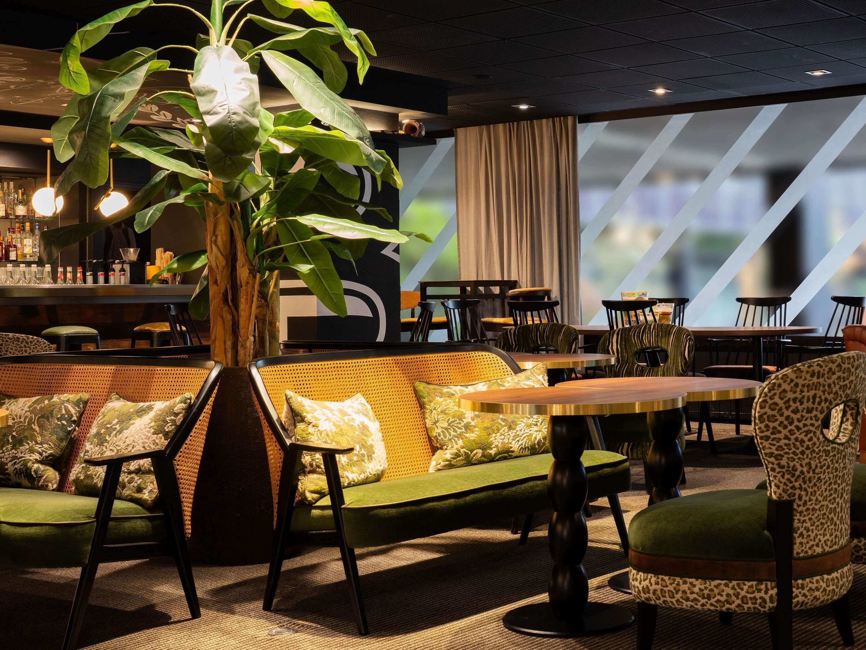 A bar area with a green sofa, patterned chairs, and a large plant.