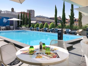 Un área de piscina en la azotea con una mesa lista para comer, rodeada de sillones de descanso y un mural en la pared.