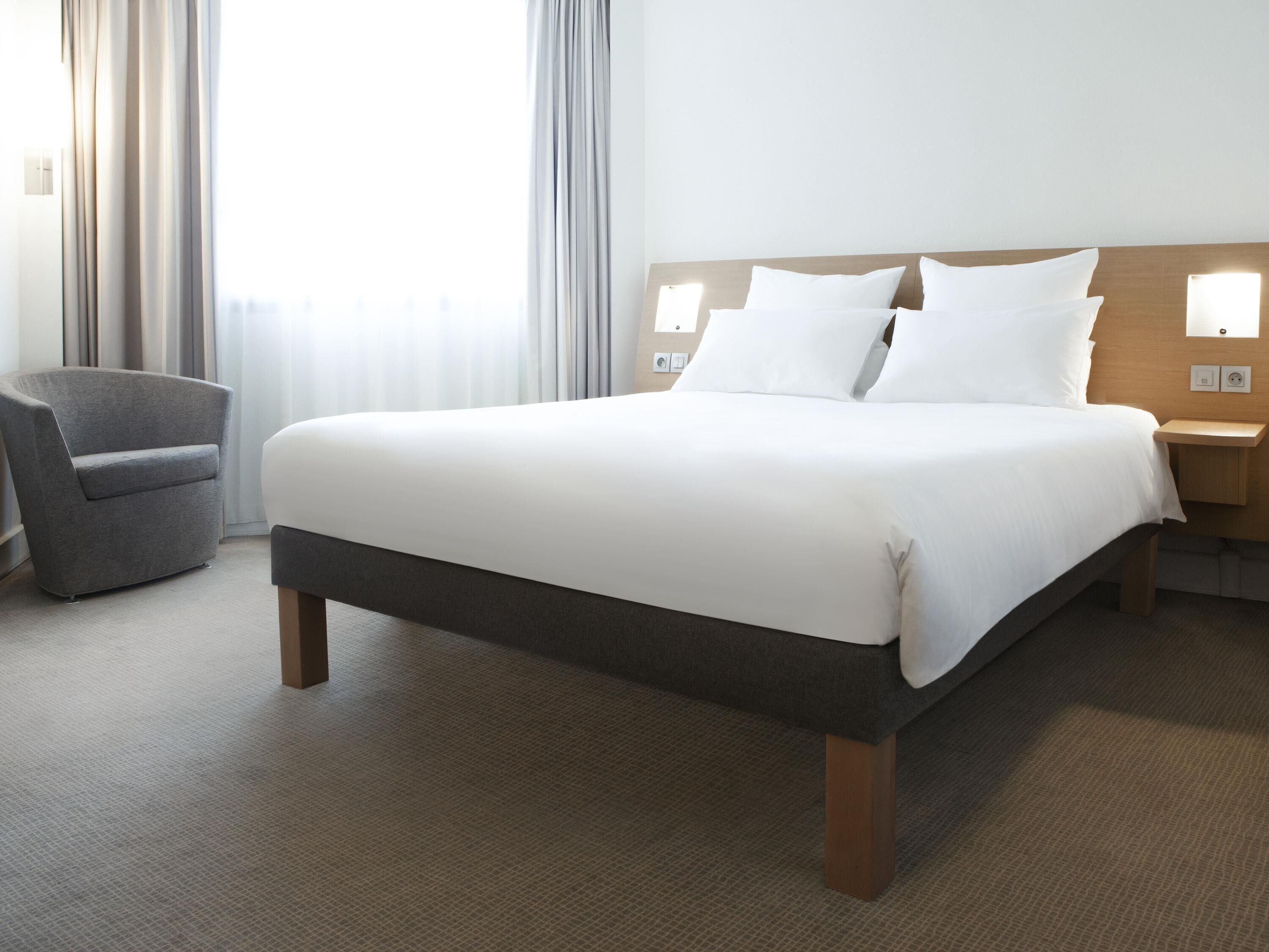 A hotel room with a large bed, a chair, and a nightstand with a lamp.