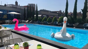 Una piscina con flotadores de cisne e flamenco inflables, rodeada de sillones de descanso y una mesa con menú.