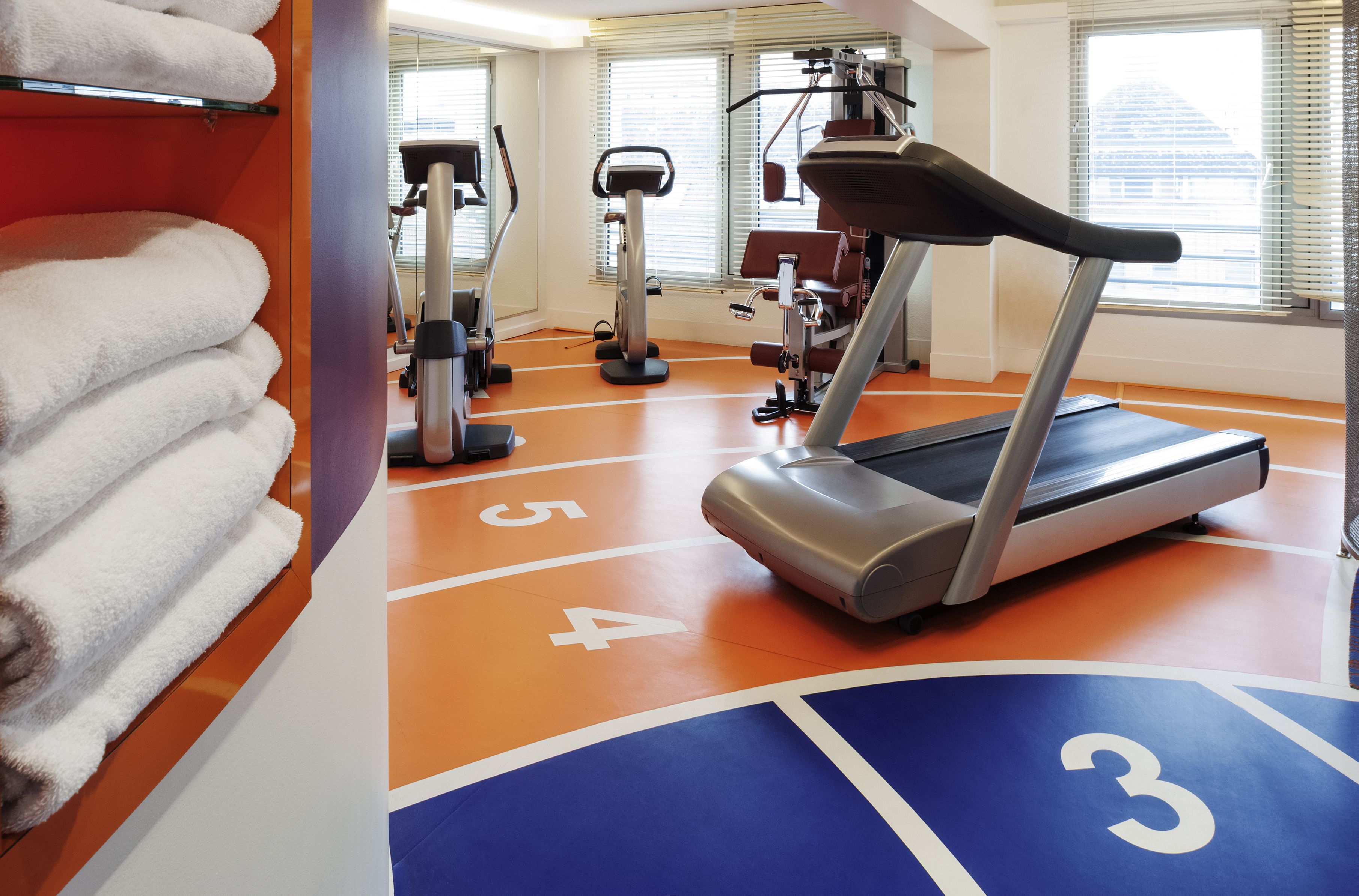 Une salle de sport équipée de matériel d’exercice, d’un tapis de course et d’un mur où sont rangées les serviettes.