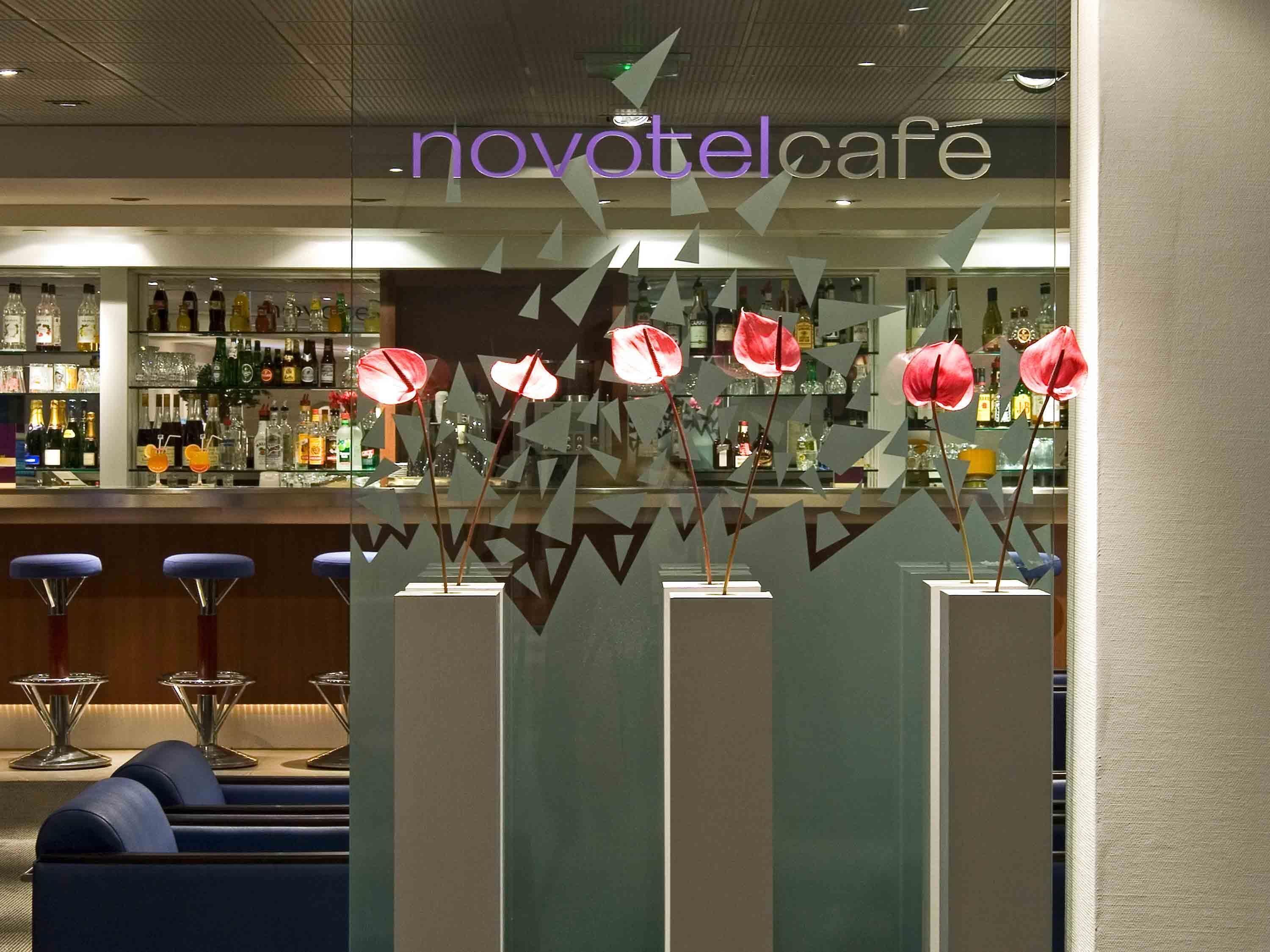 Eine Bar mit einem 'Novotel Cafe'-Schild, Barhocker und Dekorationselementen.