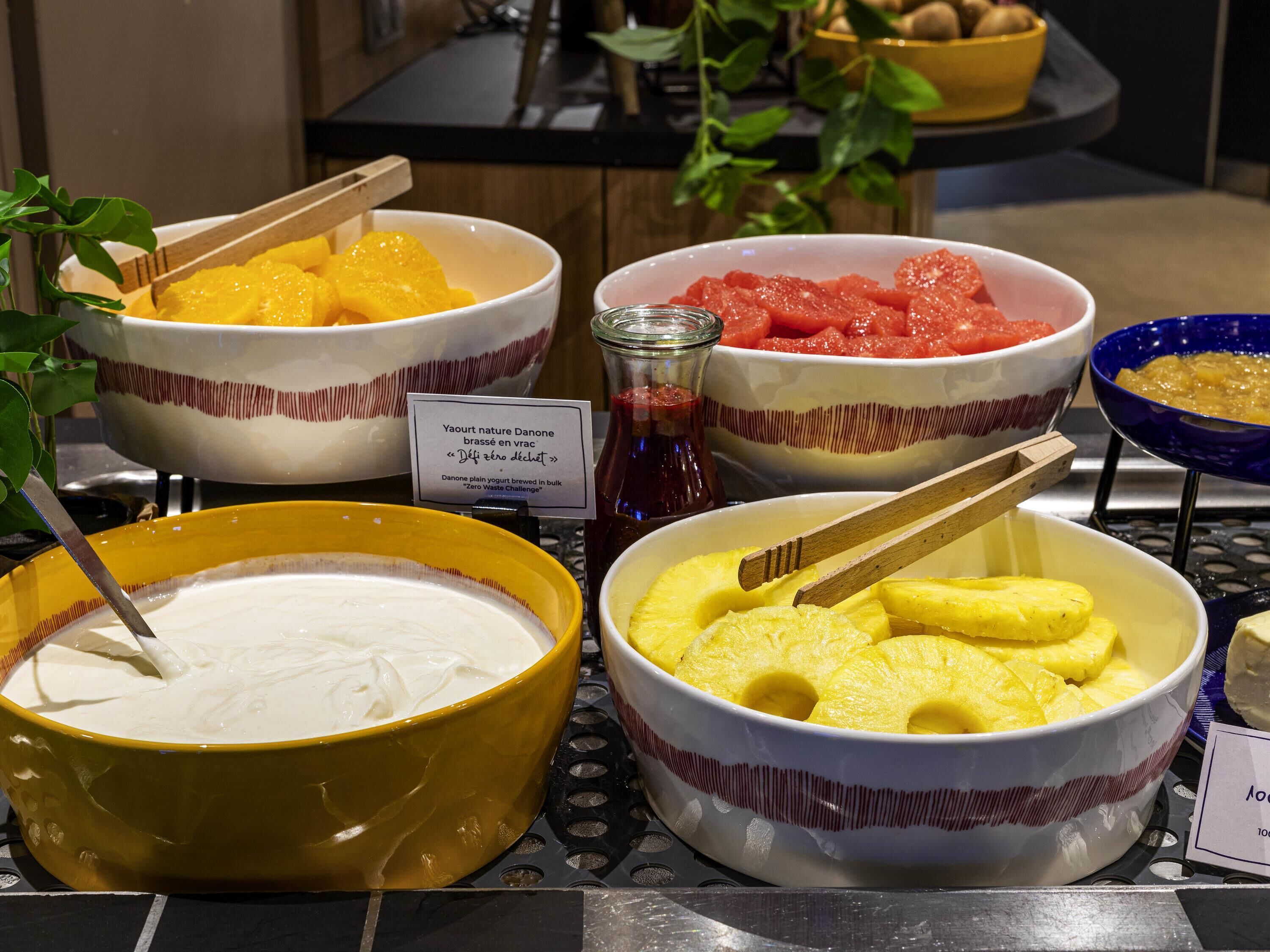 Een buffet met schalen yoghurt, ananas, watermeloen en ander fruit.