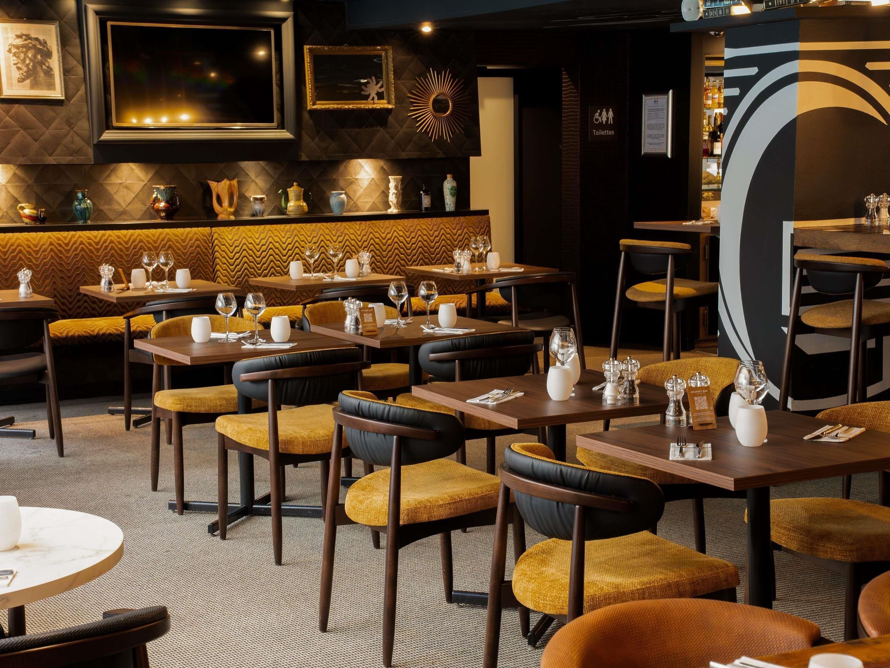 A restaurant interior with multiple dining tables and chairs, a bar area, and a wall-mounted clock.