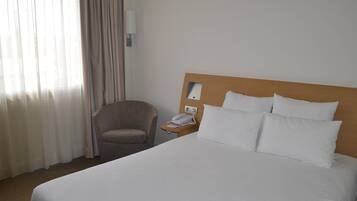 Habitación de hotel con cama, sillón, mesita de noche con teléfono y lámpara de pared.