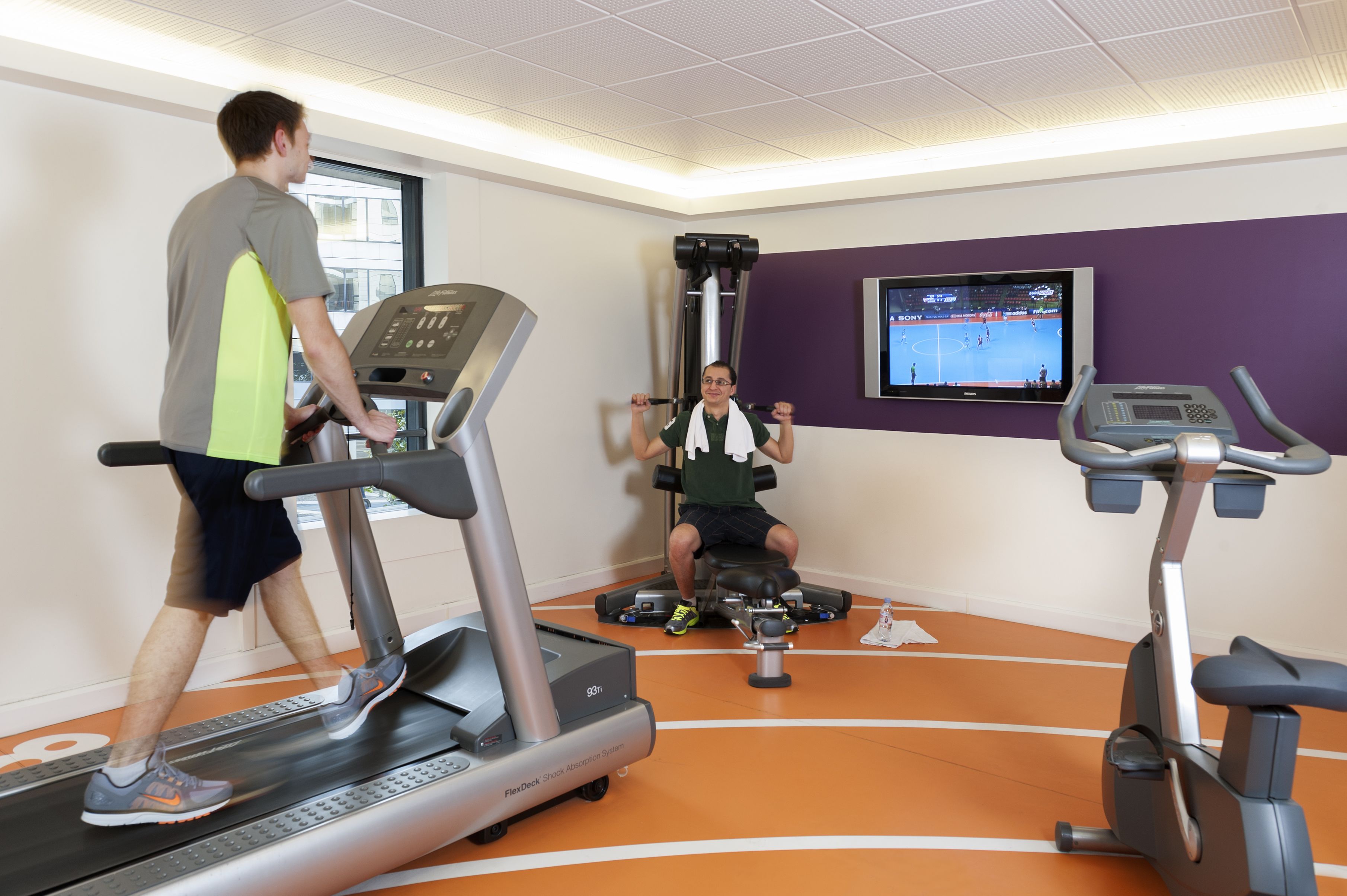 Un gimnasio con cintas de correr, una bicicleta estática y una banca para pesas.