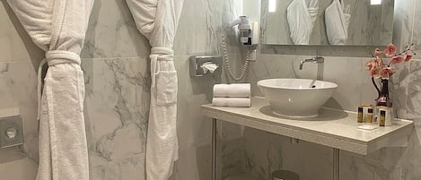 A modern bathroom with marble walls, a large mirror, a sink, and two white bathrobes hanging on hooks.