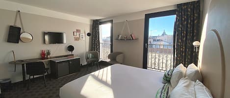 Een hotelkamer met een bed, bureau, stoel, televisie en een balkon met uitzicht.