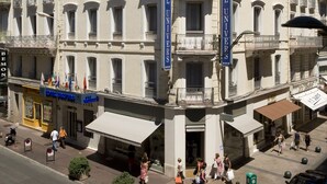 A multi-story hotel with balconies, flags, and a clear blue sky. - Hôtel Cannes Centre Univers (Cannes)