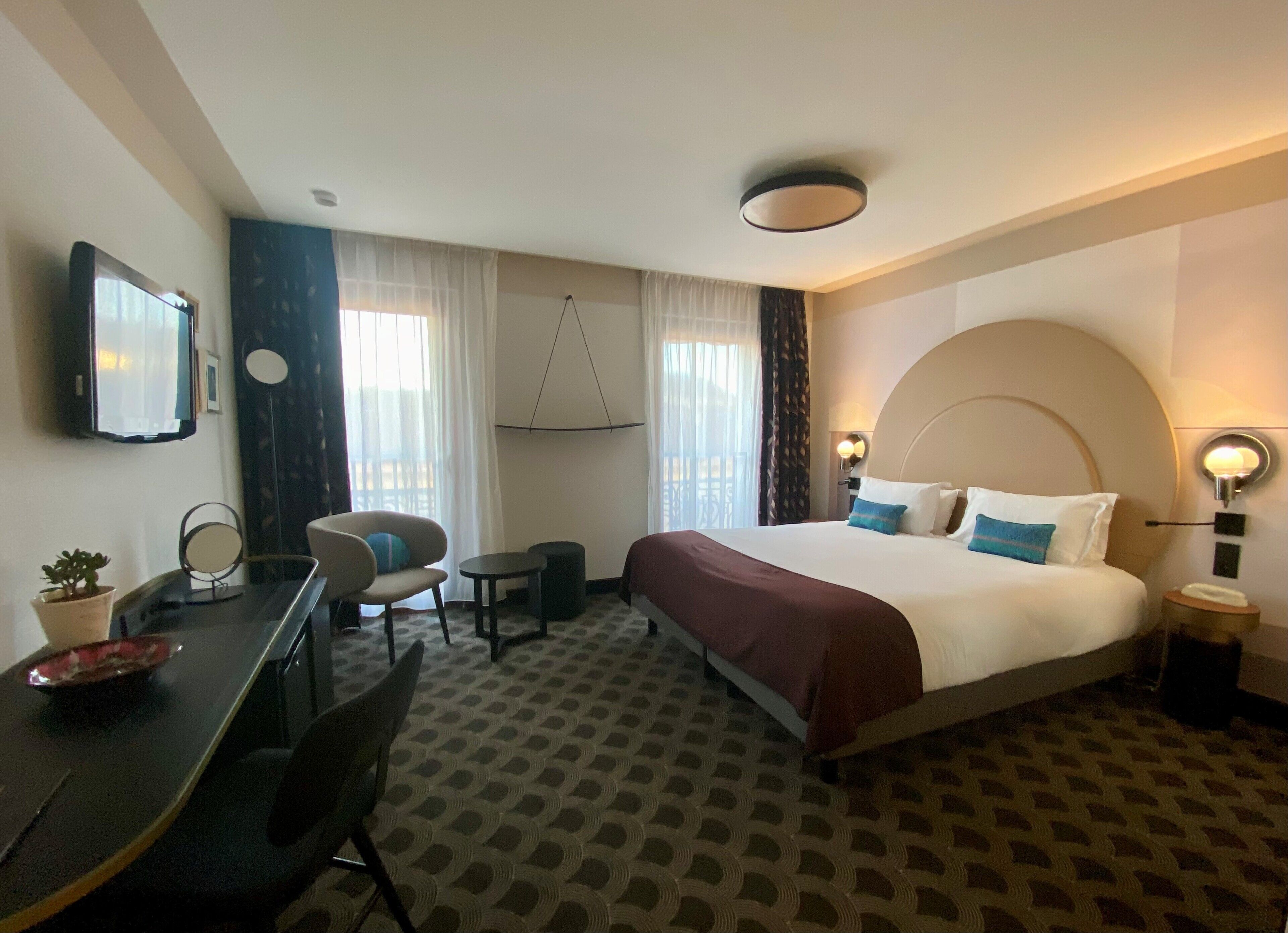 Habitación de hotel con cama, escritorio, silla, televisor y una mesita con una planta.