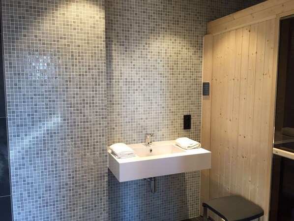 A bathroom with a tiled wall, a white sink, and a wooden panel. - Hôtel Cannes Centre Univers (Cannes)