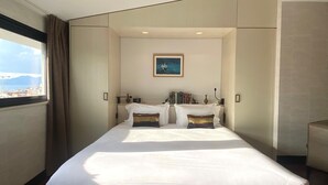 A modern hotel room with a large bed, a view of the city through the window, and a framed picture on the wall. - Hôtel Cannes Centre Univers (Cannes)