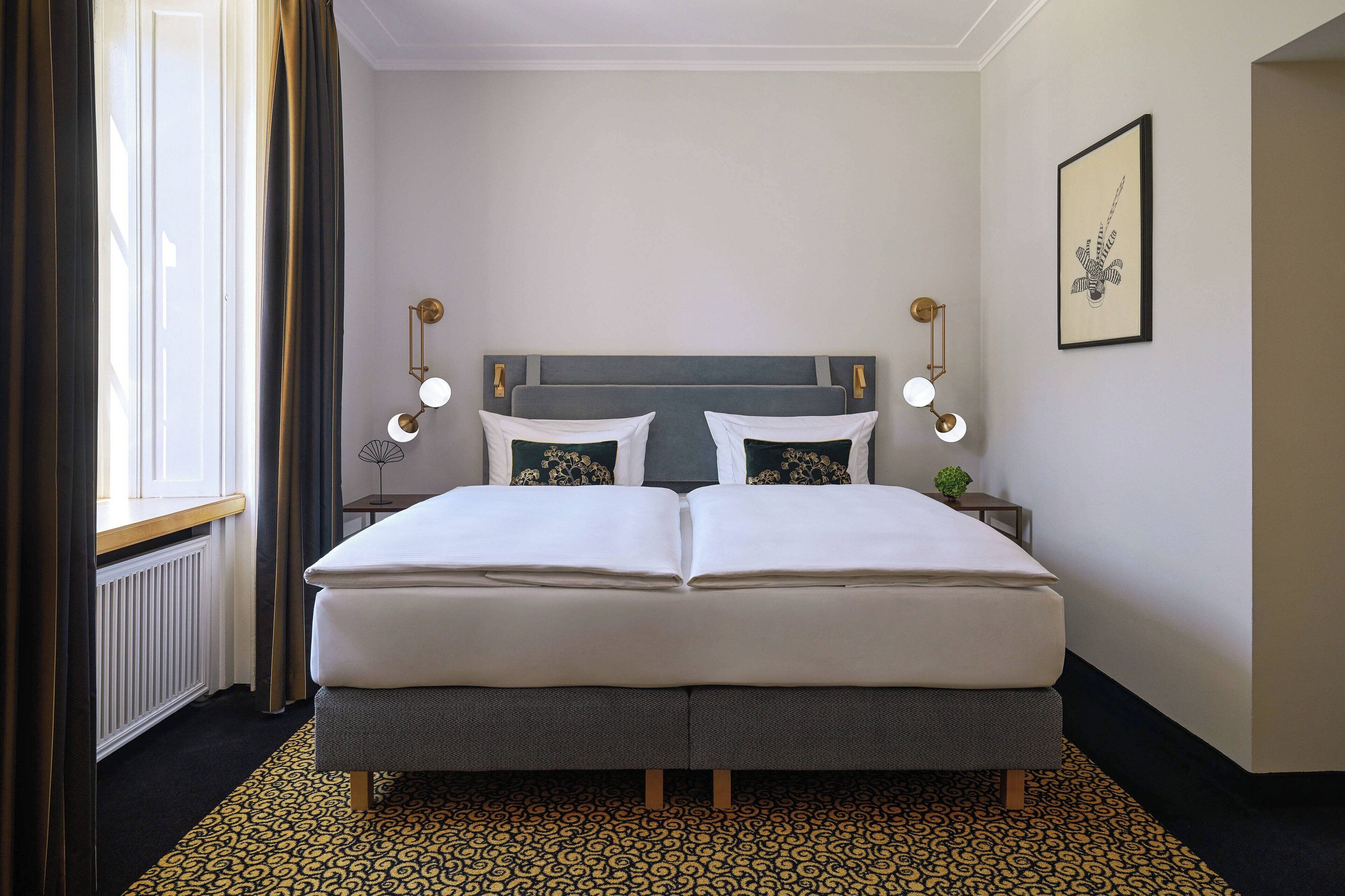 A double bed with a grey headboard, two bedside tables with lamps, a framed picture on the wall, and a patterned rug.