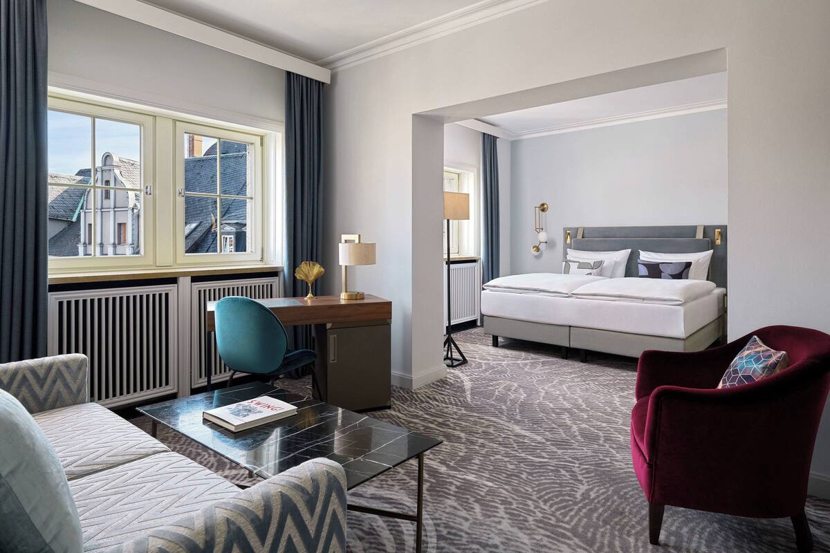 Une chambre d’hôtel avec un lit, un bureau, une chaise, un canapé et une vue sur les bâtiments par la fenêtre.