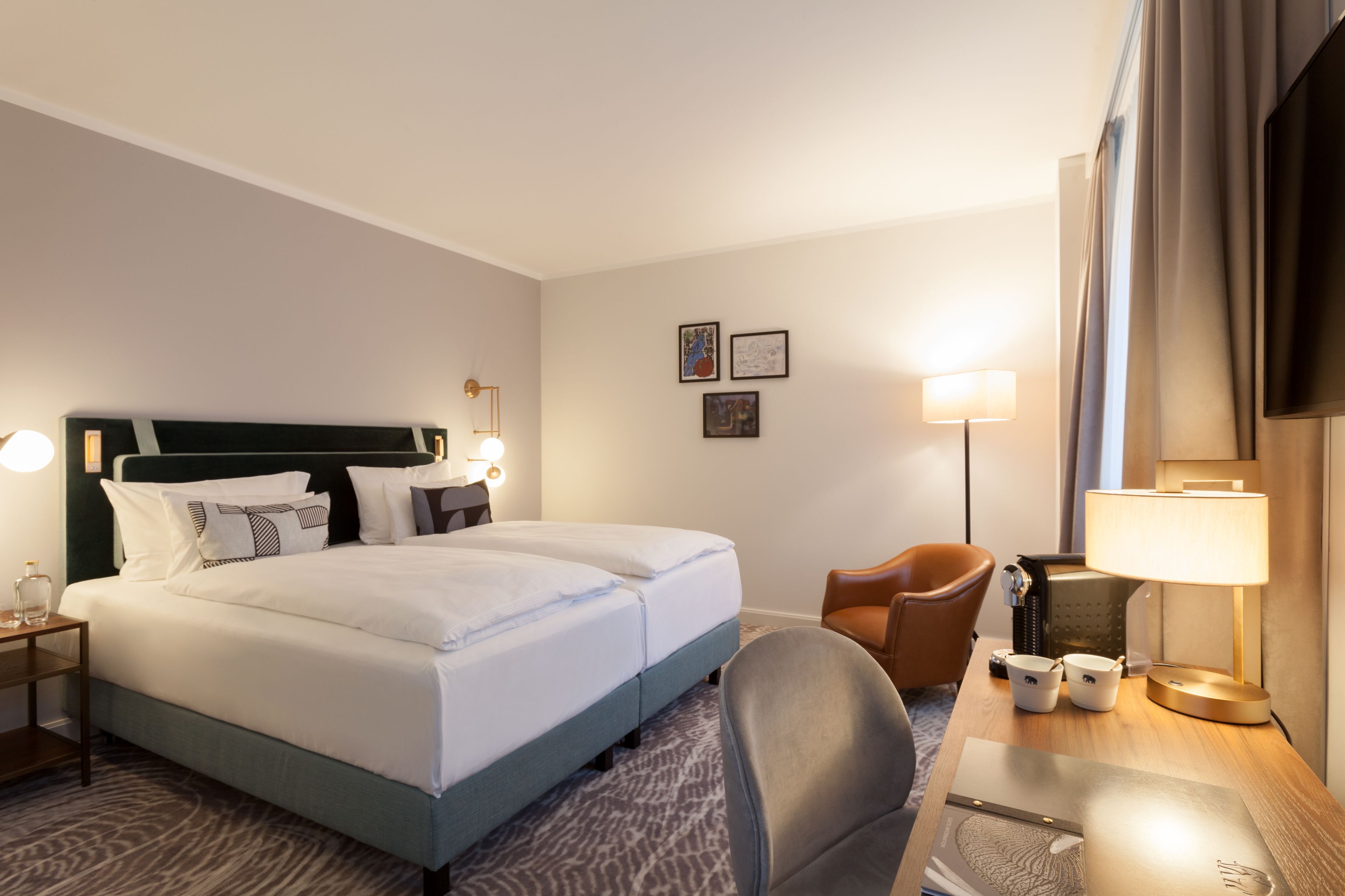 A hotel room with a large bed, two bedside tables with lamps, a desk with a chair, and a TV.