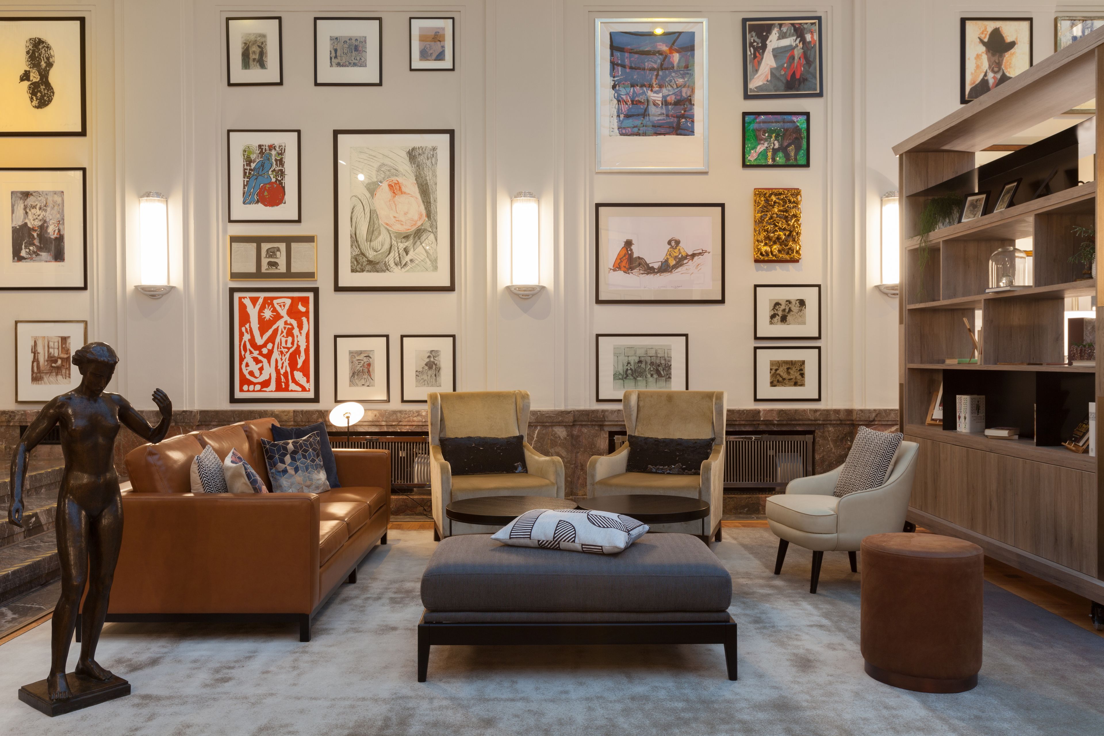 A modern living room with a sofa, armchairs, and a coffee table, surrounded by framed artworks on the walls.