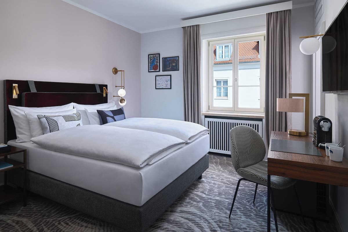 Une chambre d’hôtel avec un grand lit, un bureau avec une lampe, une chaise et une fenêtre avec des rideaux.