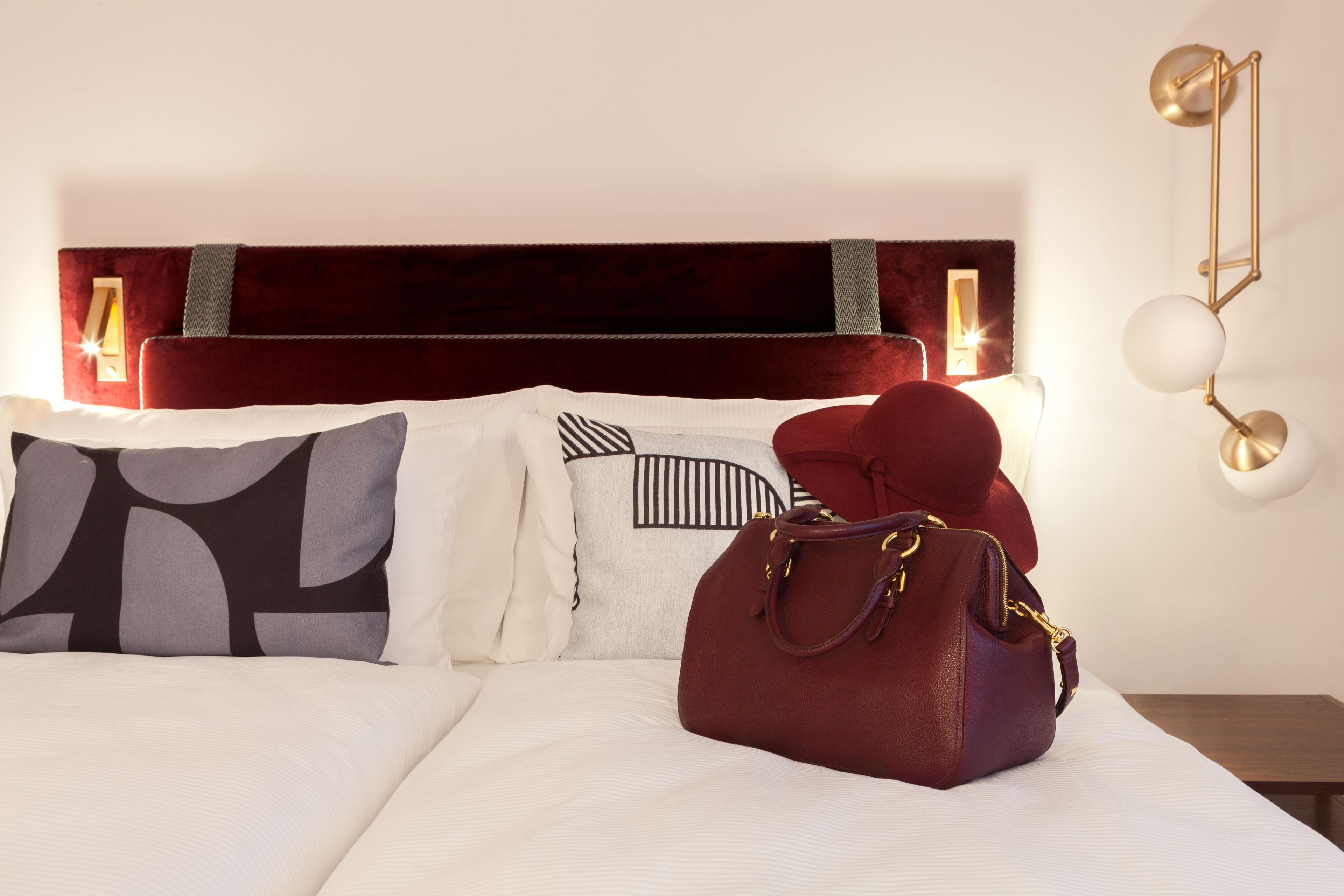 A neatly made bed with a red headboard, two pillows with geometric patterns, and a maroon handbag on the bed.