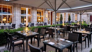 An outdoor dining area with tables and chairs, surrounded by greenery and a building with large windows. - Hotel Elephant Weimar, Autograph Collection (Weimar)