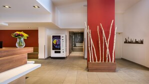 A reception area with a wooden desk, a vase of flowers, a wall-mounted heater, and a decorative plant arrangement. - Sure Hotel by Best Western Muenchen Hauptbahnhof (Munich)