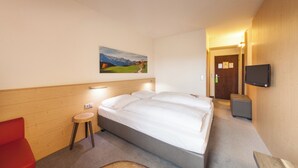 Una habitación de hotel con una cama, un taburete pequeño, un televisor y un cuadro en la pared.