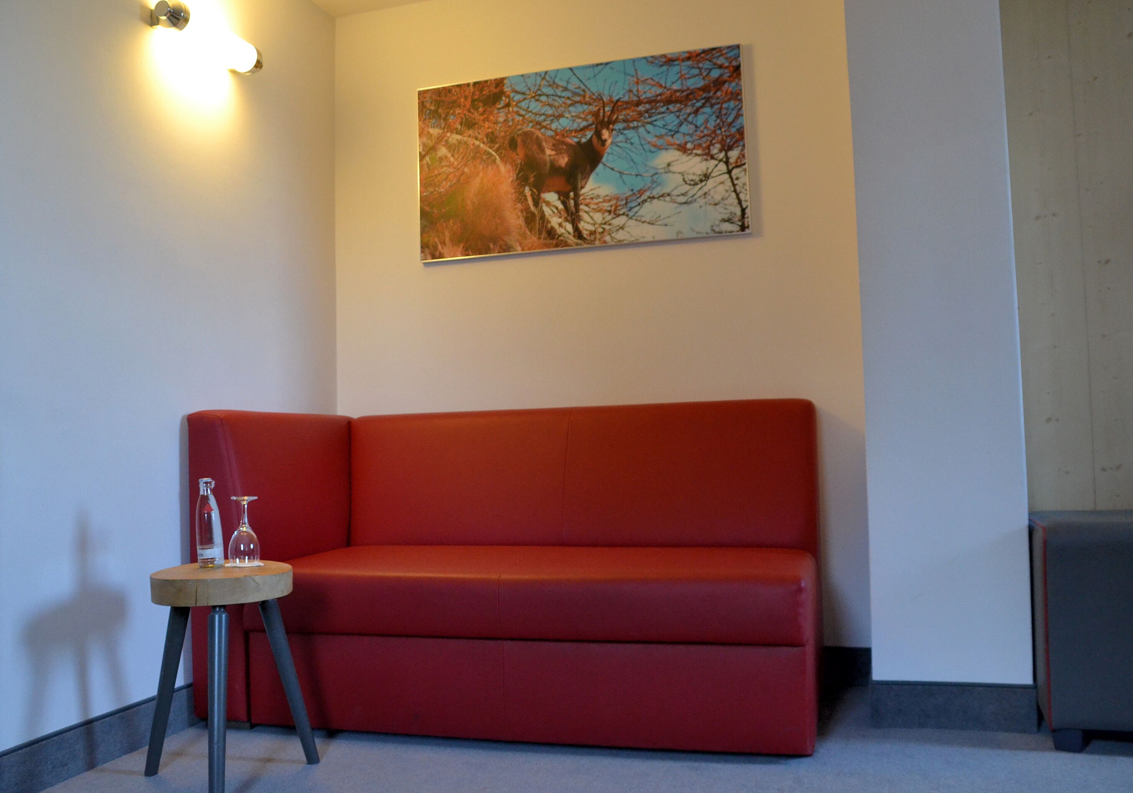 A red sofa, a small table with a glass, and a painting on the wall.