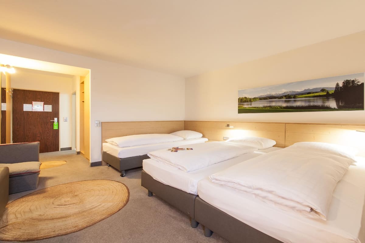 A hotel room with two beds, a desk, a chair, and a painting of a landscape.