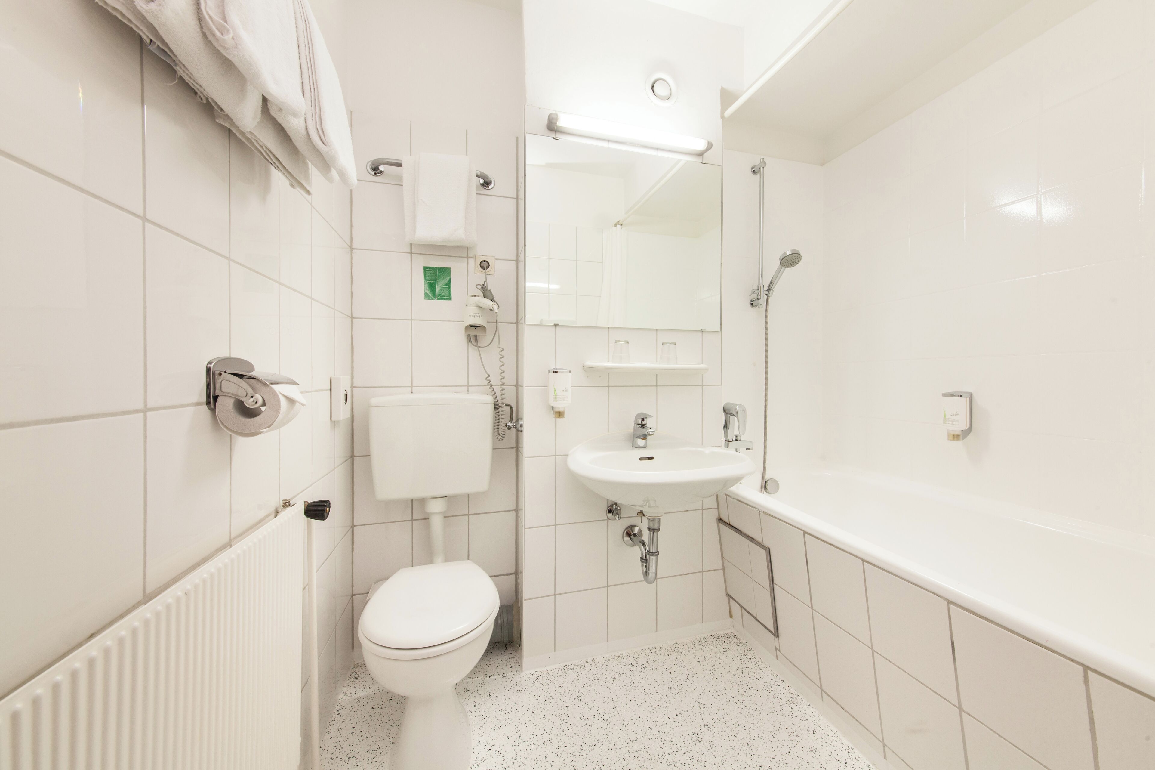 A small, modern bathroom with white tiles, a toilet, a sink, and a bathtub.
