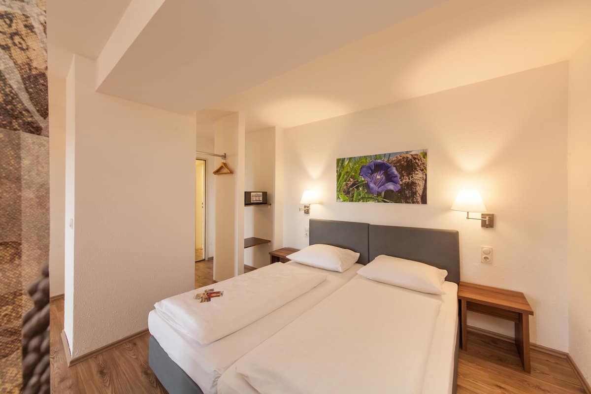 A double bed with white linens, a wooden headboard, two bedside tables with lamps, and a framed picture on the wall.