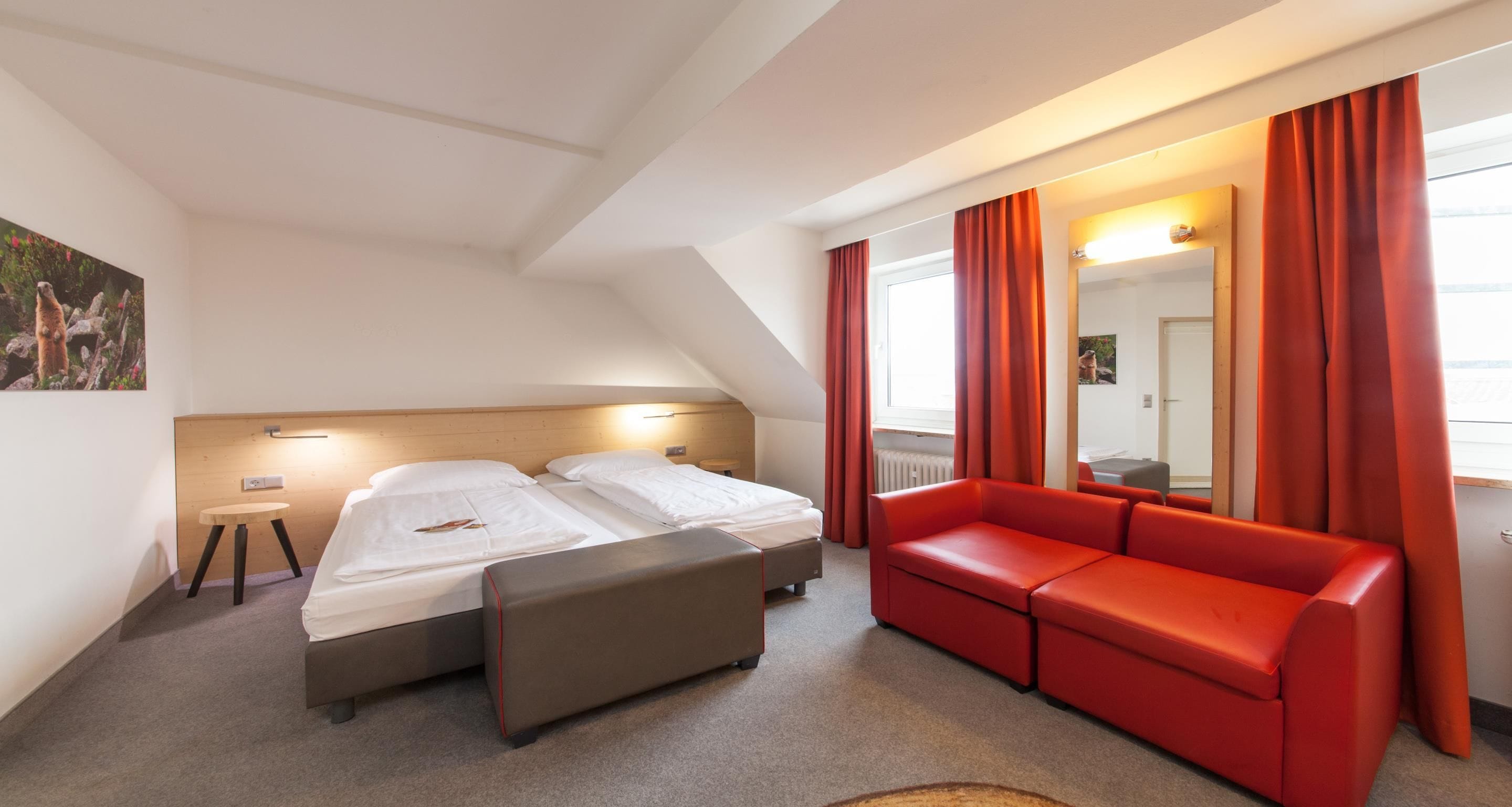 Una habitación de hotel con una cama, un sofá rojo, una mesita y un espejo.