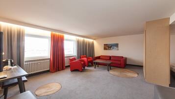 A modern hotel room with a red sofa, a small table, and a large window with curtains.
