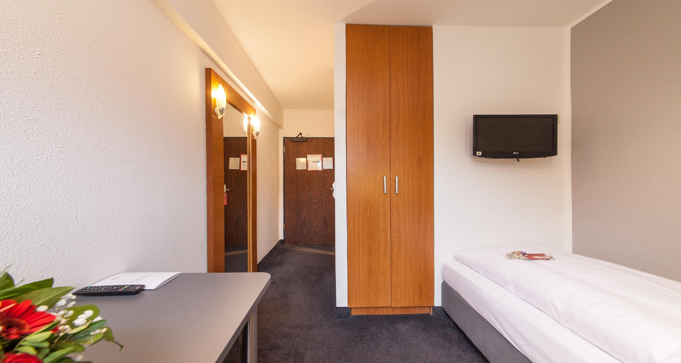 Habitación de hotel con cama, televisor montado en la pared, escritorio con control remoto y armario de madera.