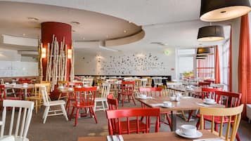 Un restaurante con mesas y sillas redondas, una pared con un mural de aves y un pilar rojo.