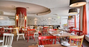 A restaurant with round tables and chairs, a wall with a bird mural, and a red pillar. - Sure Hotel by Best Western Muenchen Hauptbahnhof (Munich)