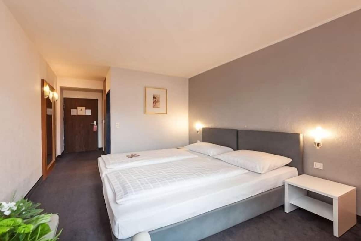 A hotel room with a bed, bedside table, and a door leading to another room.