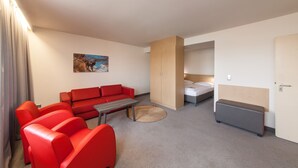 Una habitación moderna con un sofá rojo, una mesita, una cama y un armario.
