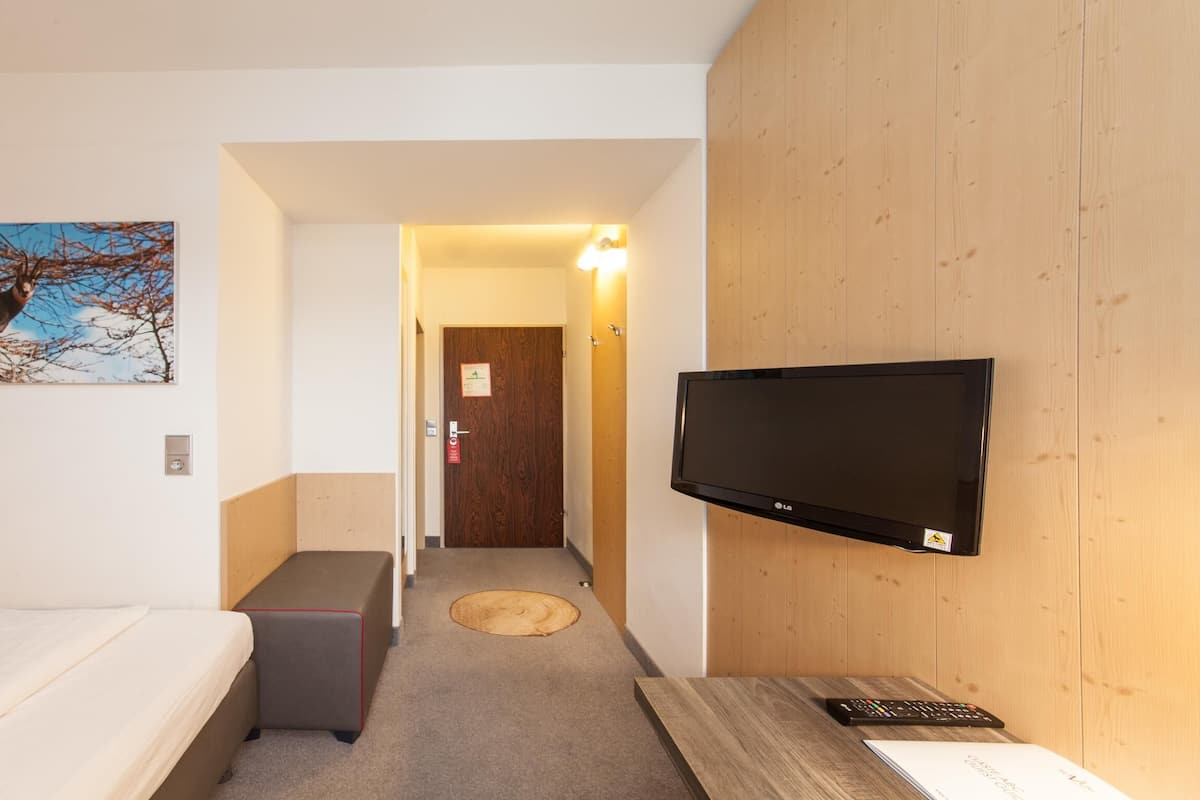 A hotel room with a bed, a bench, a flat-screen TV mounted on the wall, and a painting of a deer.
