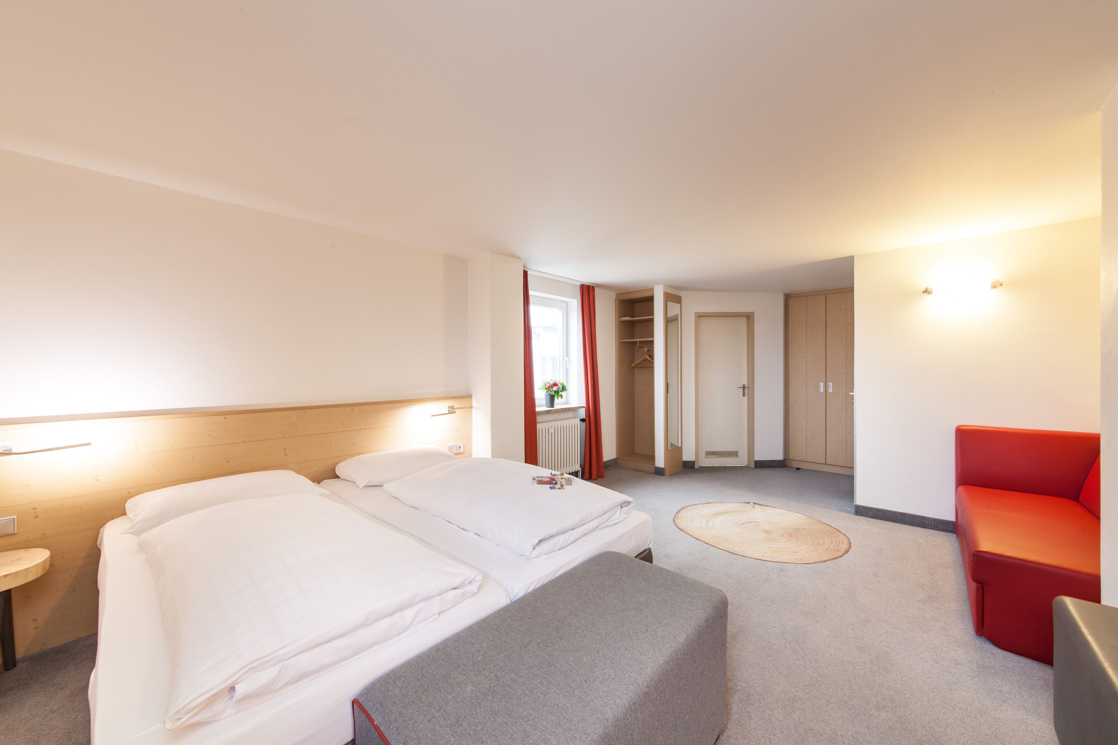 A hotel room with two beds, a red sofa, a small table, and a mirror.