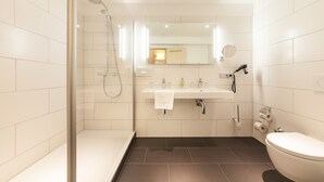 Un baño moderno con ducha de vidrio, lavamanos blanco y espejo superior, además de un inodoro.