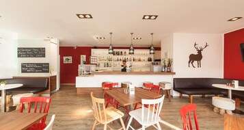 Un interno ristorante con zona bar, tavoli in legno, sedie rosse e un adesivo decorativo a forma di cervo sulla parete.