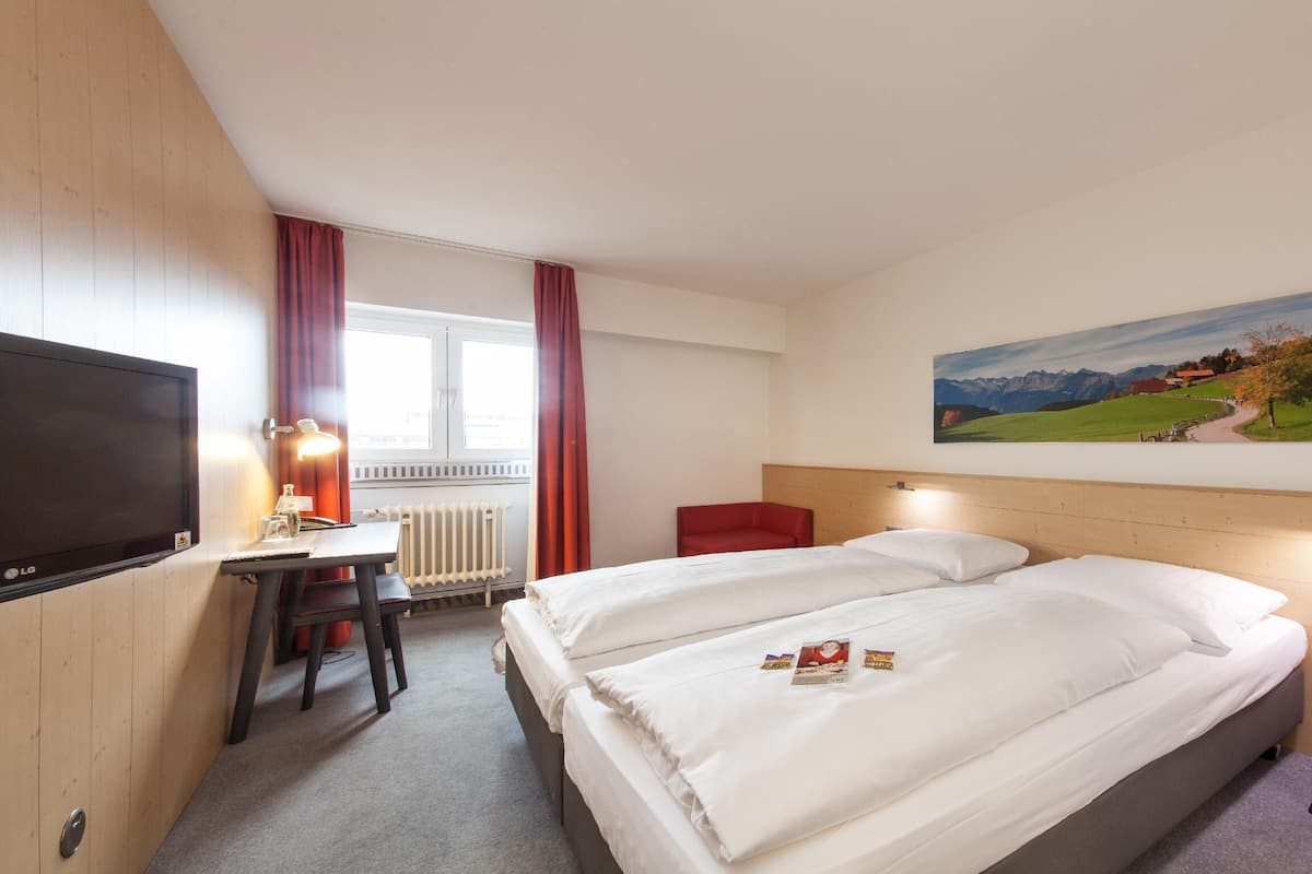 A hotel room with a bed, a desk with a computer, a TV, and a painting of a landscape.