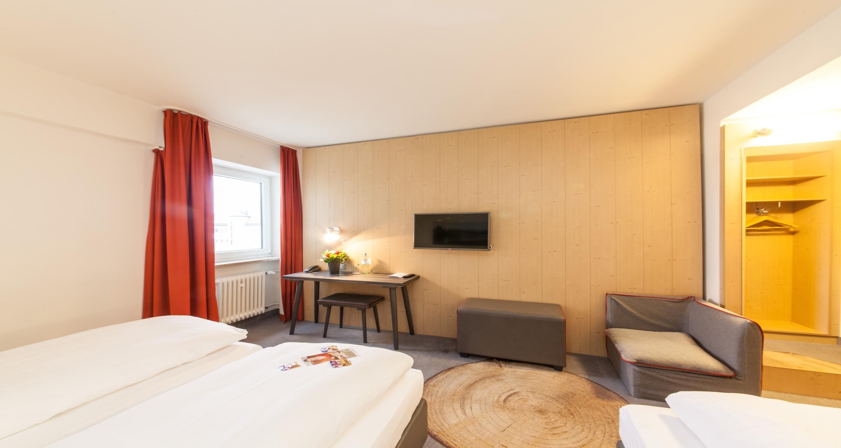 Una habitación de hotel con cama, escritorio con silla, televisor y panel de pared de madera.