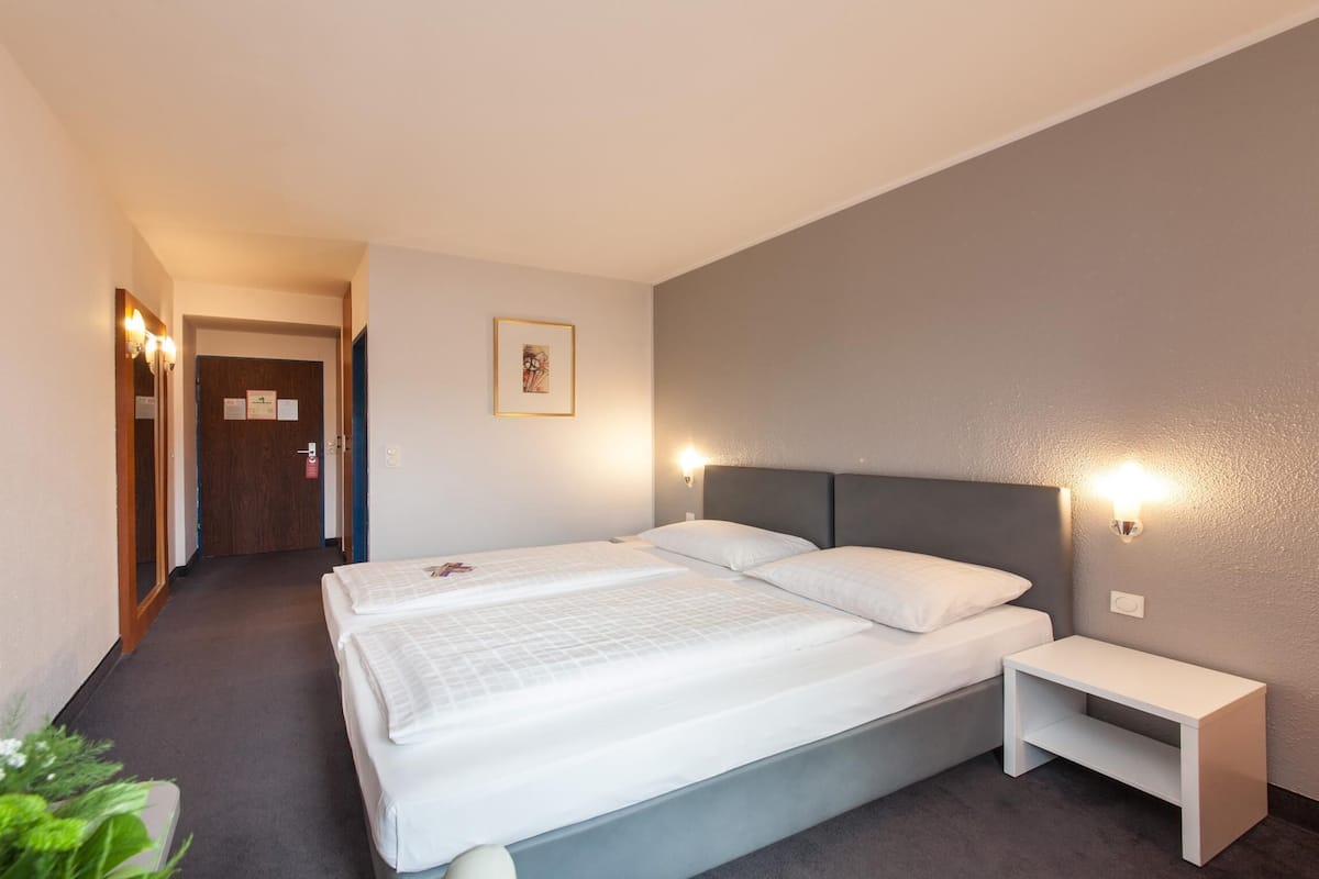 A hotel room with a double bed, a bedside table, a nightstand, and a wall-mounted light.