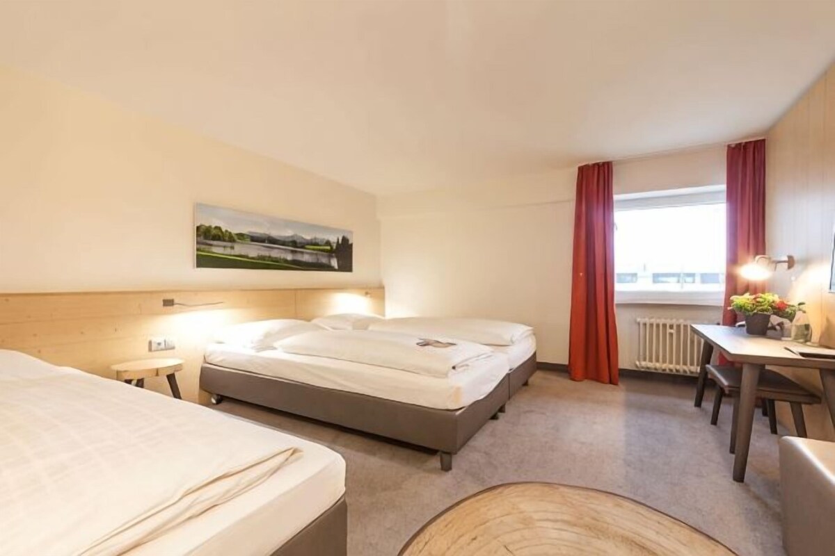 A hotel room with two beds, a desk, a chair, a window with curtains, and a painting on the wall.