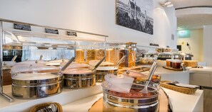 Zona de buffet con varios recipientes de comida y un letrero que indica diferentes tipos de yogur.