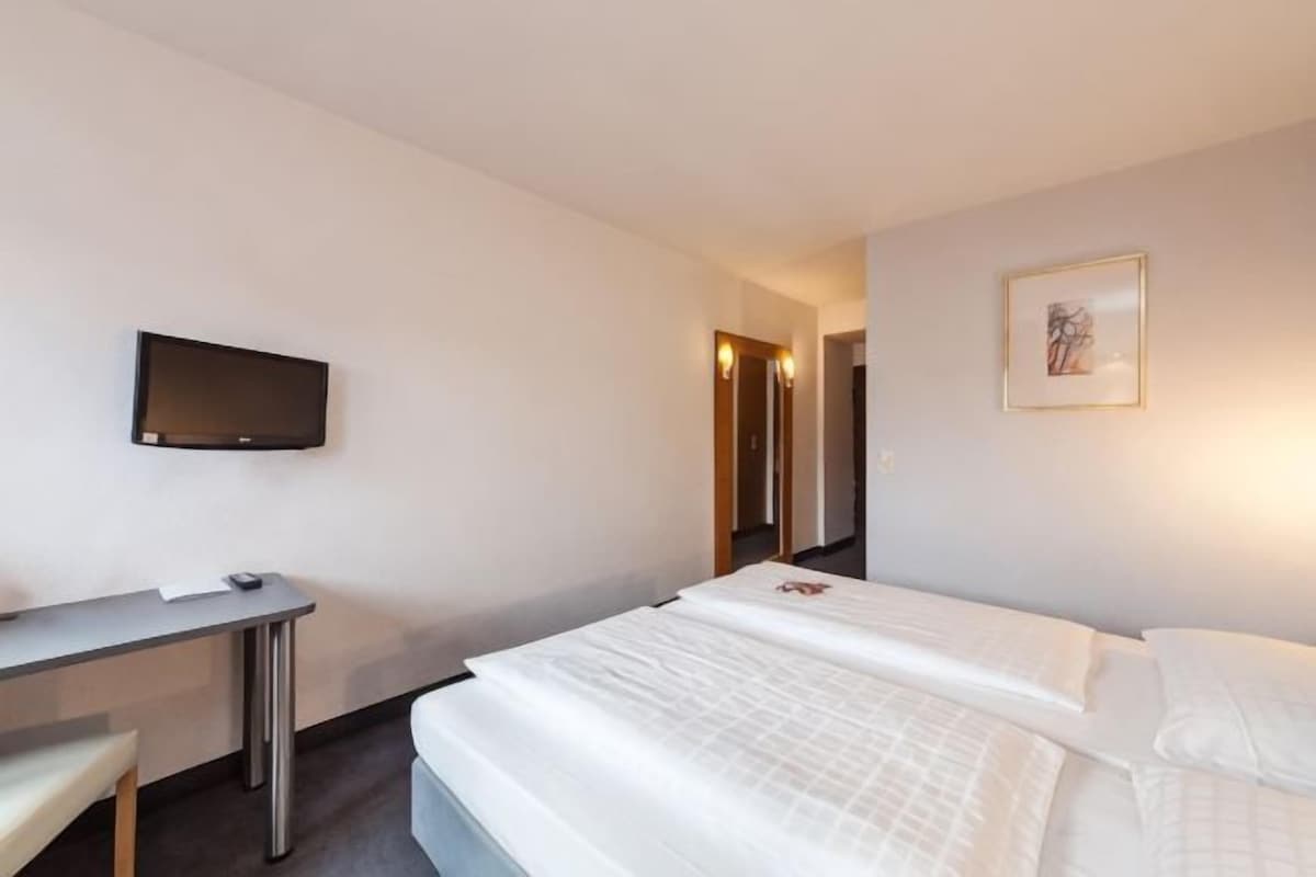 A hotel room with a bed, a desk, a chair, a television, and a framed picture on the wall.