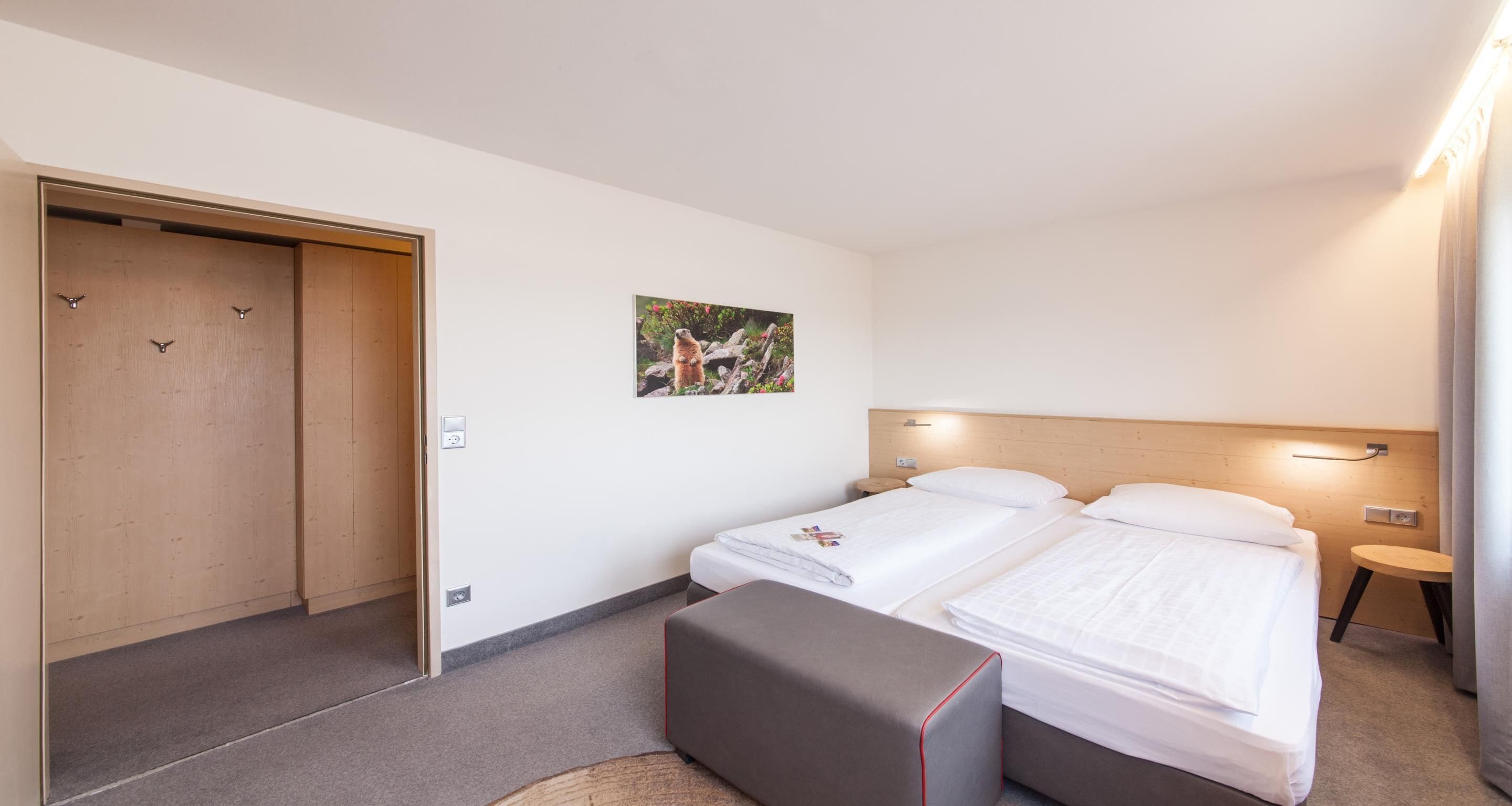 A hotel room with two beds, a wooden wardrobe, a small round table, and a wall-mounted light fixture.