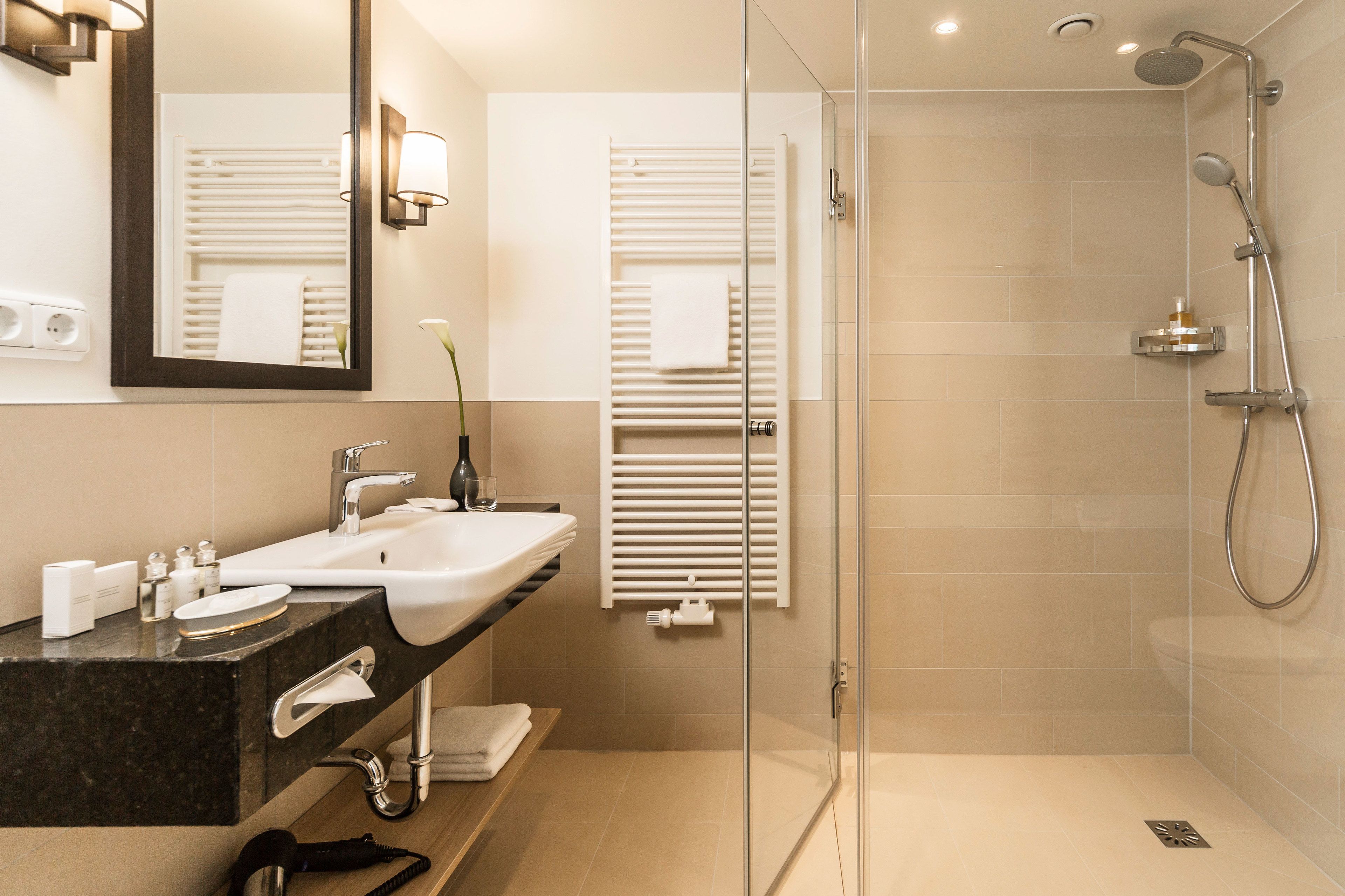 Un baño moderno con ducha de vidrio, lavamanos con encimera de mármol e iluminación empotrada en la pared frente al espejo.
